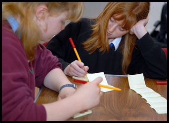 2 teenage girls sat at a table writing