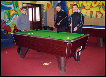 3 teenage boys standing round a pool table.